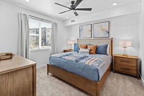 A bedroom with a bed, two bedside tables, a ceiling fan, and a window with blinds.