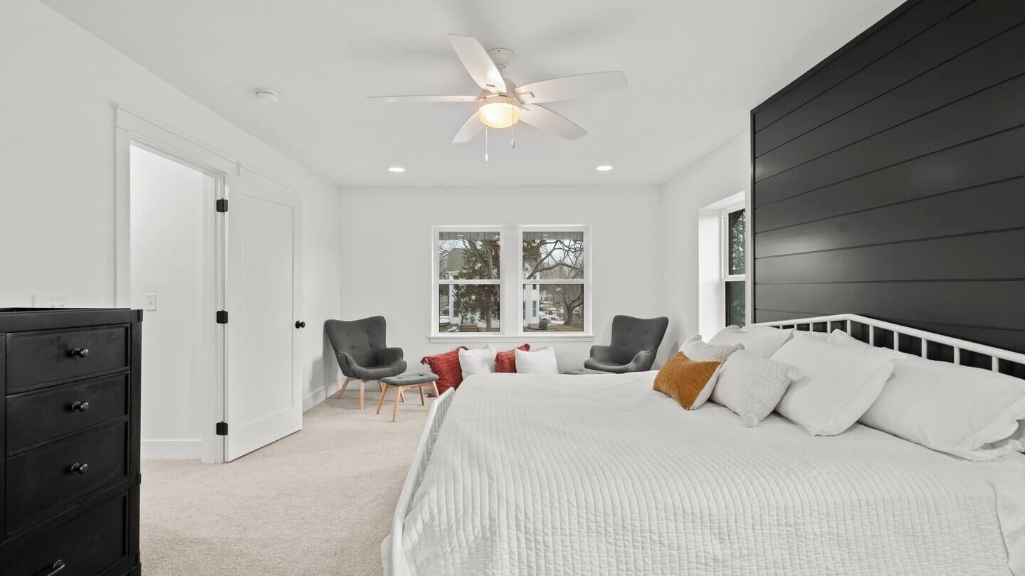 Une chambre avec un grand lit, un ventilateur de plafond, une fenêtre donnant sur un beau paysage et un mur de couleur sombre.