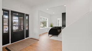 Ein modernes Interieur mit einer schwarzen Tür, einem Wohnbereich mit einer Couch und einer Treppe.