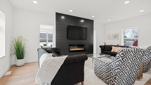 A modern living room with a fireplace, two sofas, a coffee table, and a TV mounted on a dark wall.