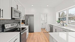 A modern kitchen with white cabinets, stainless steel appliances, and a large window.