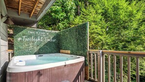 Un bain à remous sur une terrasse en bois, agrémentée d’une balustrade en bois, le tout entouré d’un luxuriant feuillage verdoyant.