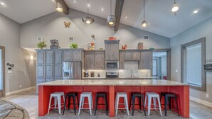 A spacious kitchen with a large island, grey cabinets, and red accents.