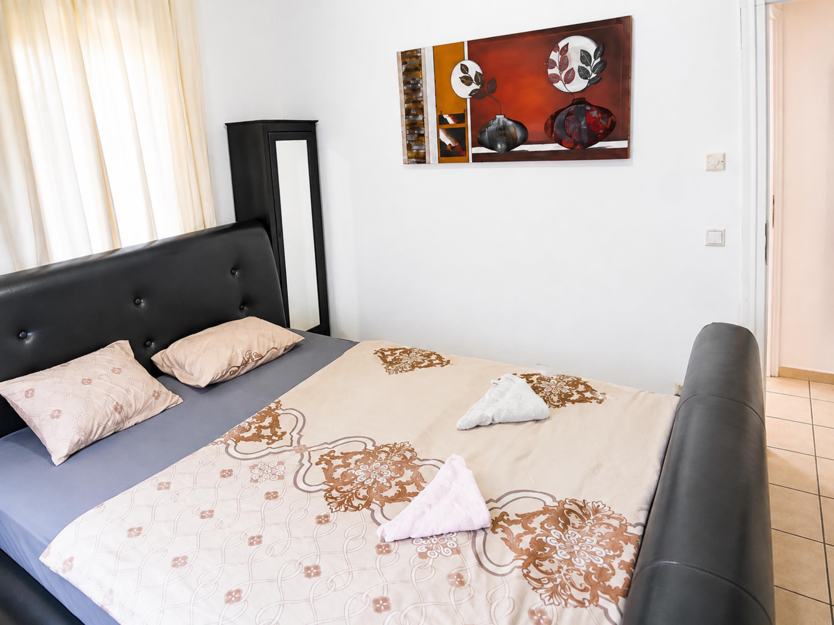 Ein Schlafzimmer mit einem Bett, Kissen, einem Nachttisch und einem Wandbild.