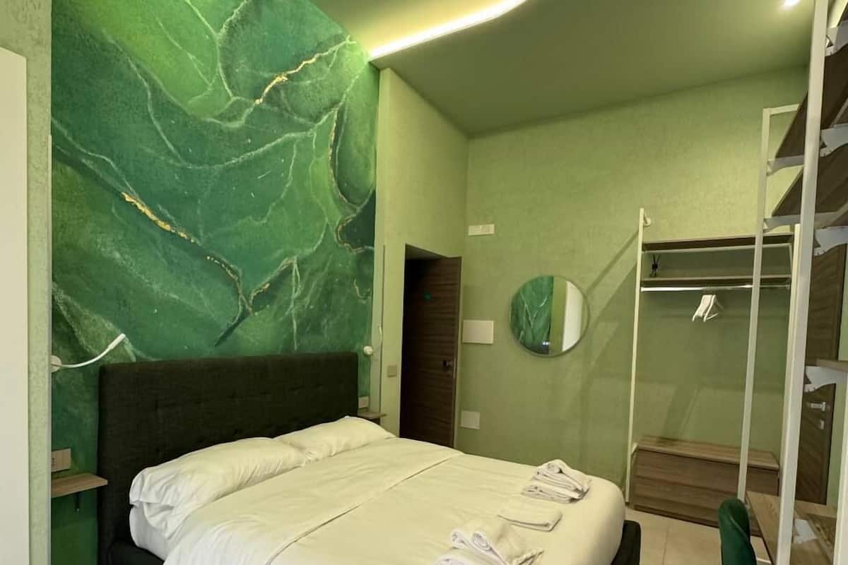 Habitación de hotel moderna con una cama, pared de mármol verde, un escritorio pequeño y una escalera.