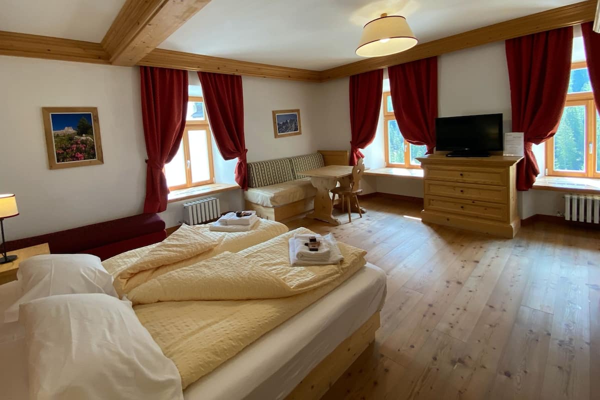 A bedroom with a large bed, a wooden dresser, a TV, and a window with red curtains.