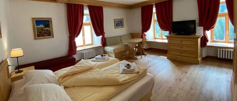 A bedroom with a large bed, a wooden dresser, a TV, and a window with red curtains.