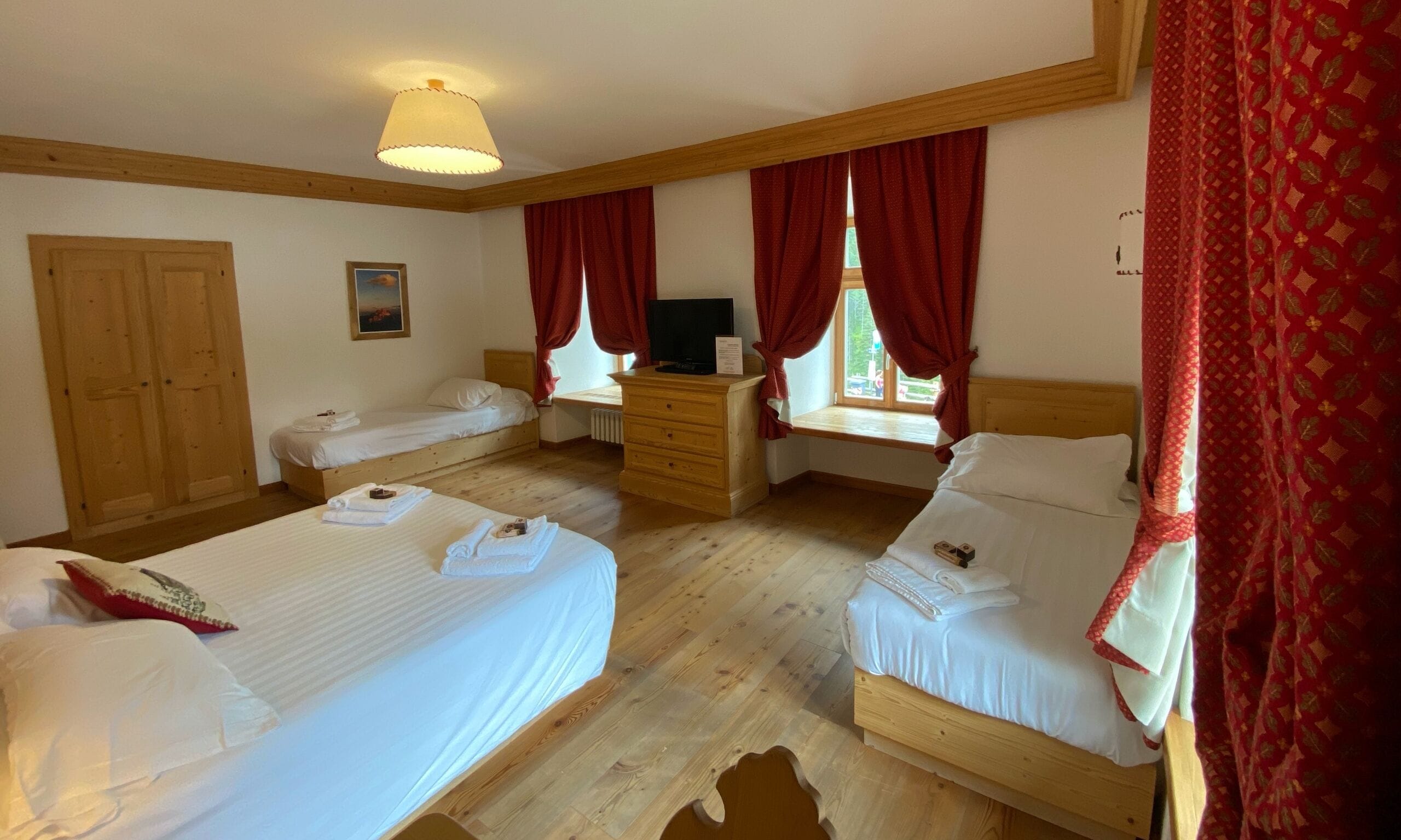 Una habitación de hotel con dos camas, un aparador de madera, un televisor y una ventana con cortinas rojas.