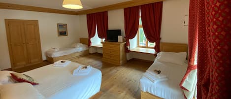 Hotellihuone, jossa on kaksi sänkyä, puinen lipasto, televisio ja ikkuna, jossa on punaiset verhot.