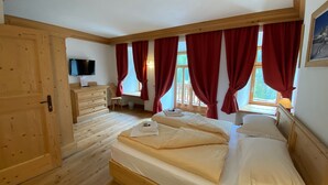 Une chambre à coucher avec un lit en bois, une commode en bois, un téléviseur et une fenêtre ornée de rideaux rouges.