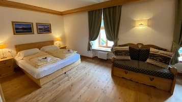 Un dormitorio con cama de madera, un sofá de madera, dos mesitas de noche, un ventanal con cortinas y dos cuadros colgados en la pared.