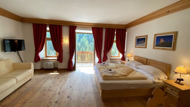 Une chambre avec un plancher en bois, un lit, une télévision et un balcon agrémenté de rideaux rouges.