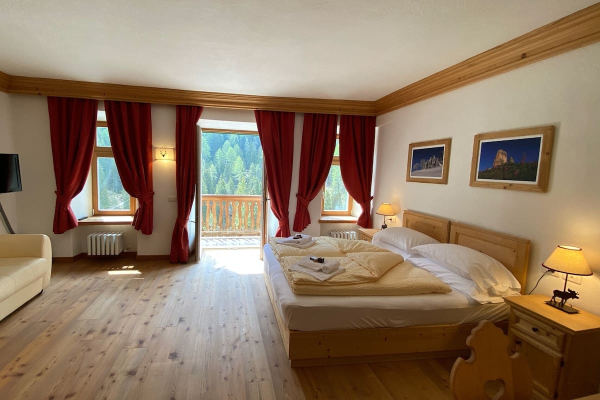 A bedroom with a wooden floor, a bed, a TV, and a balcony with red curtains.