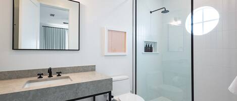 Un baño moderno con cabina de ducha de vidrio, lavabo con encimera de mármol y retrete.