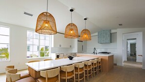 A modern kitchen with a central island, pendant lights, and a view of the outdoors. - The Joyrise House at Solaire Lunara Bay (Key West)