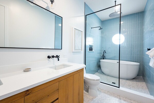 A modern bathroom with a large mirror, a white sink, a wooden vanity, a glass-enclosed shower, and a freestanding bathtub.