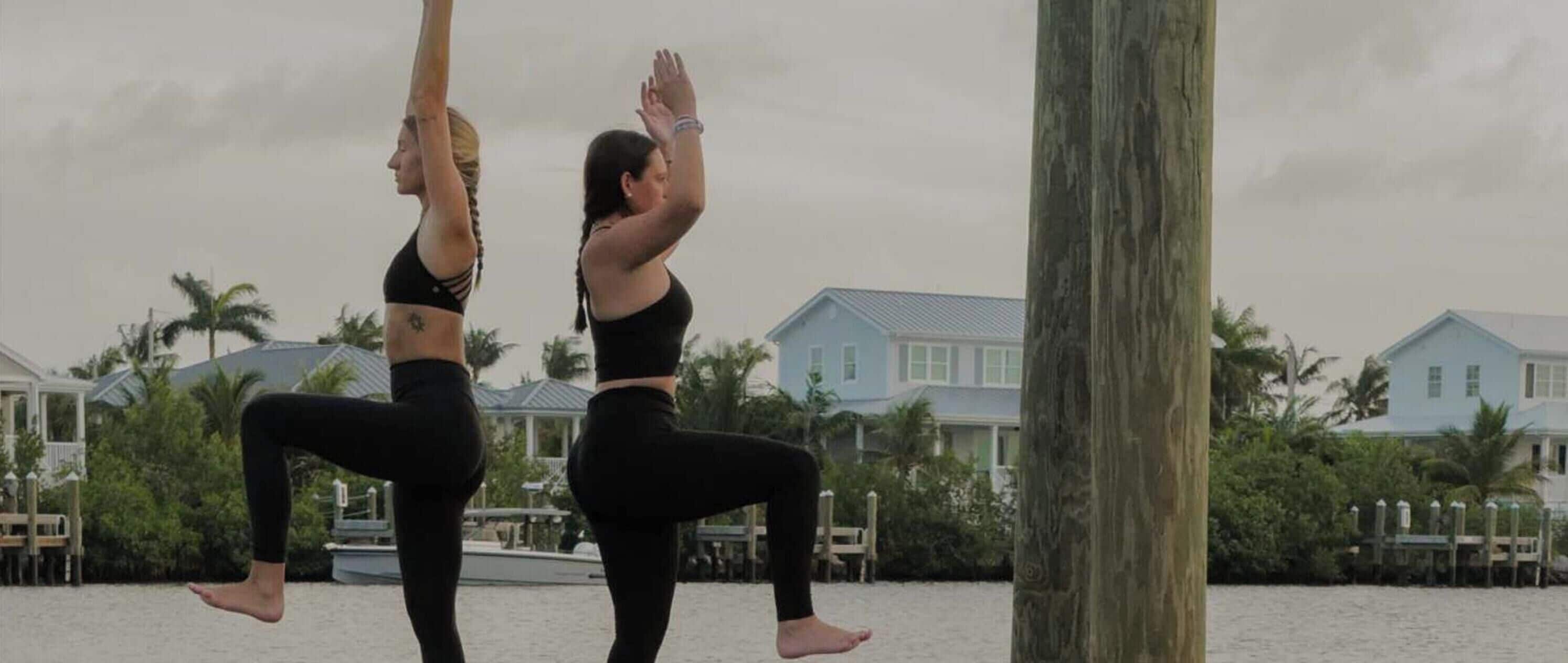 Two individuals performing a yoga pose outdoors with a residential area in the background.
