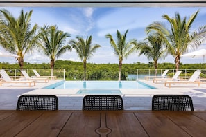 A poolside area with lounge chairs, a wooden table, and palm trees.