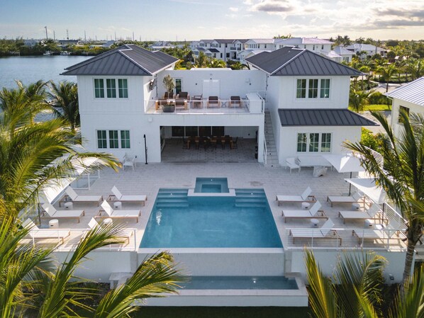 A large, two-story house with a swimming pool surrounded by lounge chairs and palm trees.