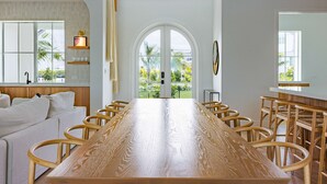 Une pièce spacieuse avec une longue table en bois, des sièges confortables, une grande fenêtre donnant sur un paysage verdoyant et un luminaire moderne.