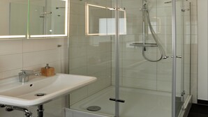 Een moderne badkamer met een douchecabine van glas, een witte wastafel en een spiegel erboven.
