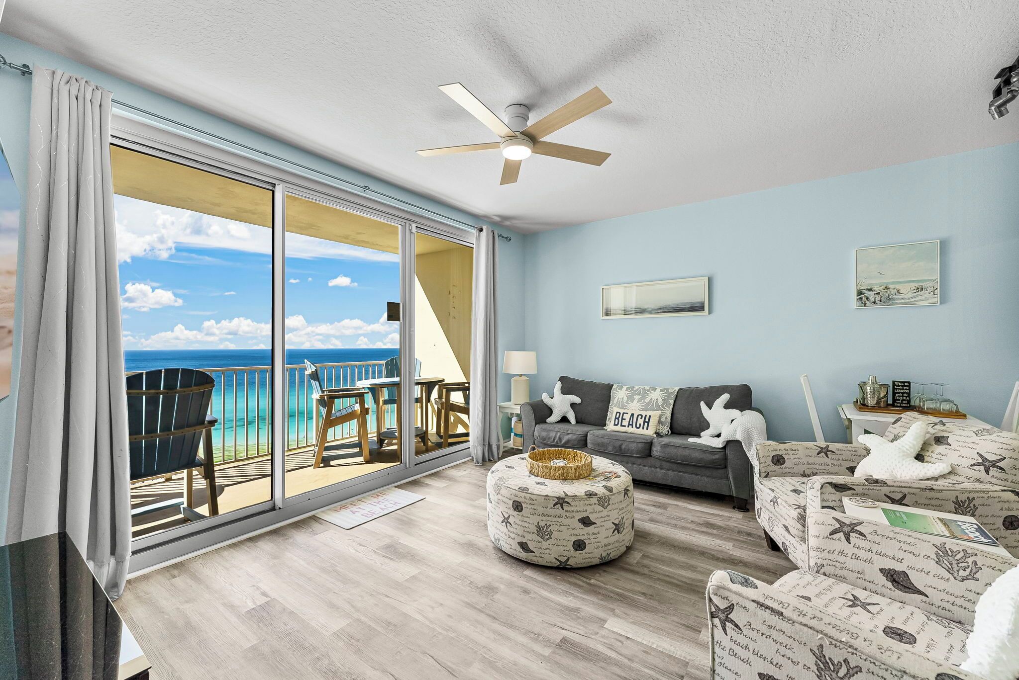 A spacious living room with a large sliding glass door leading to a balcony with a view of the ocean.