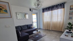 A living room with a dark-colored sofa, a round coffee table, and a large window with curtains.