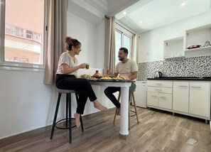 A modern kitchen with a dining area, a window with curtains, and a view of a building outside. - Hamilton Suites & Appart (Casablanca)