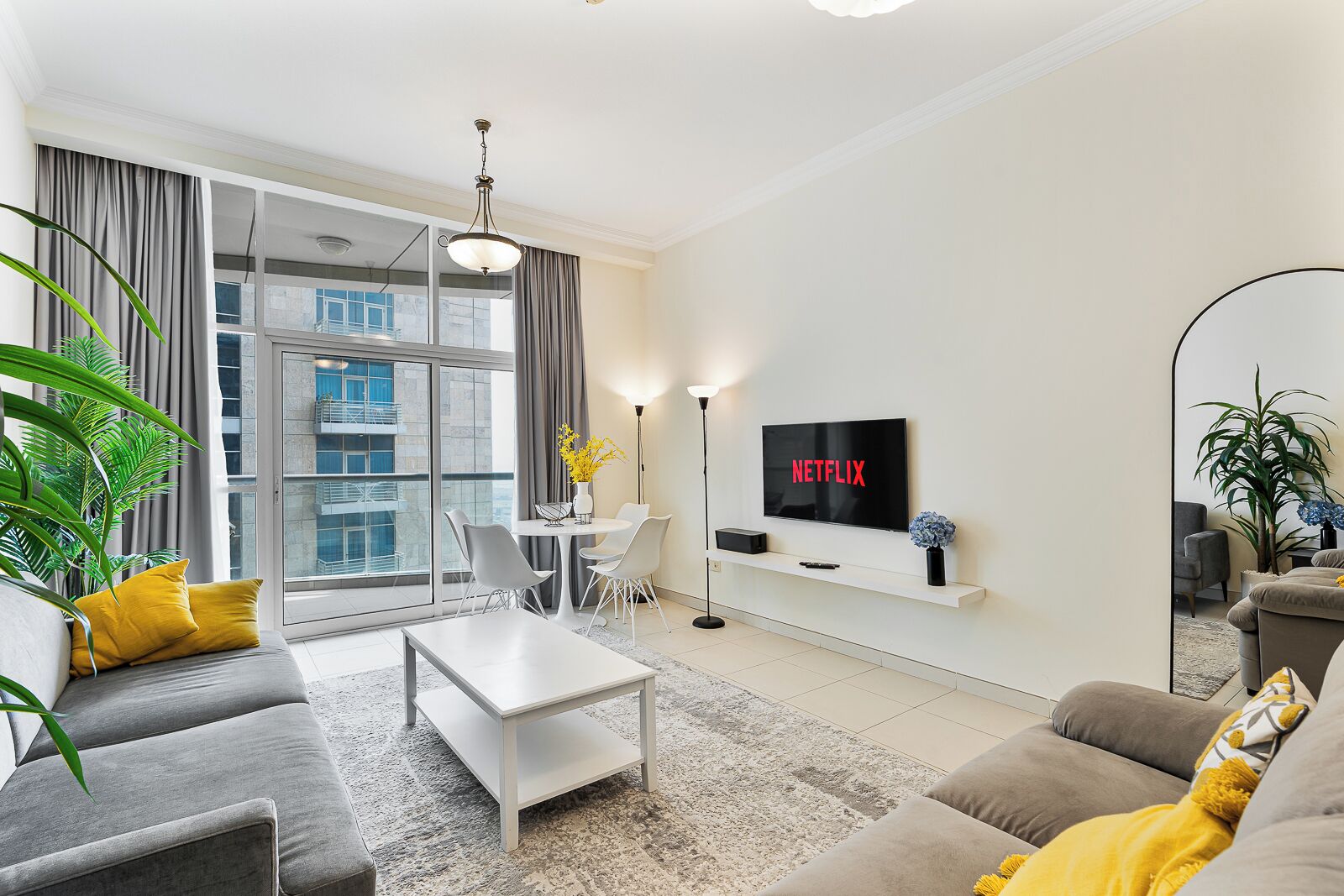 A modern living room with a flat-screen TV, a dining area, and large windows.