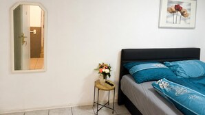 Un dormitorio con cama, una mesita de noche con un florero, un cuadro en la pared y un espejo que refleja la habitación.