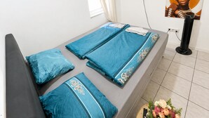 Una cama individual con ropa de cama azul, un televisor de pantalla plana montado en la pared y un cartel de una persona.