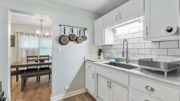 A modern kitchen with white cabinets, a stainless steel sink, and a hanging pot rack.