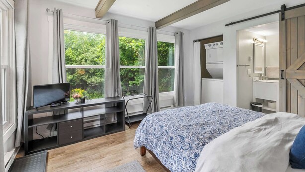 Ein Schlafzimmer mit einem Bett, einem Schreibtisch mit Fernseher, einem Herd und großen Fenstern.
