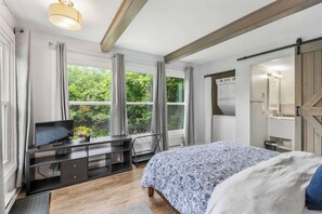 Ein Schlafzimmer mit einem Bett, einem Schreibtisch mit Fernseher, einem Herd und großen Fenstern.