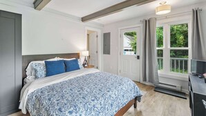 Ein Schlafzimmer mit Bett, Schreibtisch, Fenster mit Vorhängen und einer Tür.