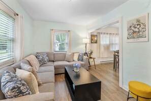 A living room with a sofa, a coffee table, a yellow chair, and a dining area with chairs and a table.