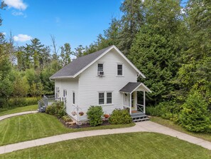 A two-story house with a front porch, surrounded by a well-maintained lawn and dense trees.