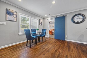A dining area with a glass table and blue upholstered chairs, a clock on the wall, and a blue sliding door leading to another room.