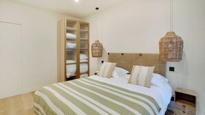 Un lit bien fait, avec une couvre-lit à rayures, une tête de lit en bois et deux appliques murales en osier.
