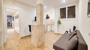 A modern living room with a grey sofa, a stone pillar, and a kitchen in the background. - Radio Suites (Rome)