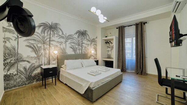 A bedroom with a bed, bedside tables, a desk, and a chair. There is a mural on the wall and a window with curtains. - Radio Suites (Rome)