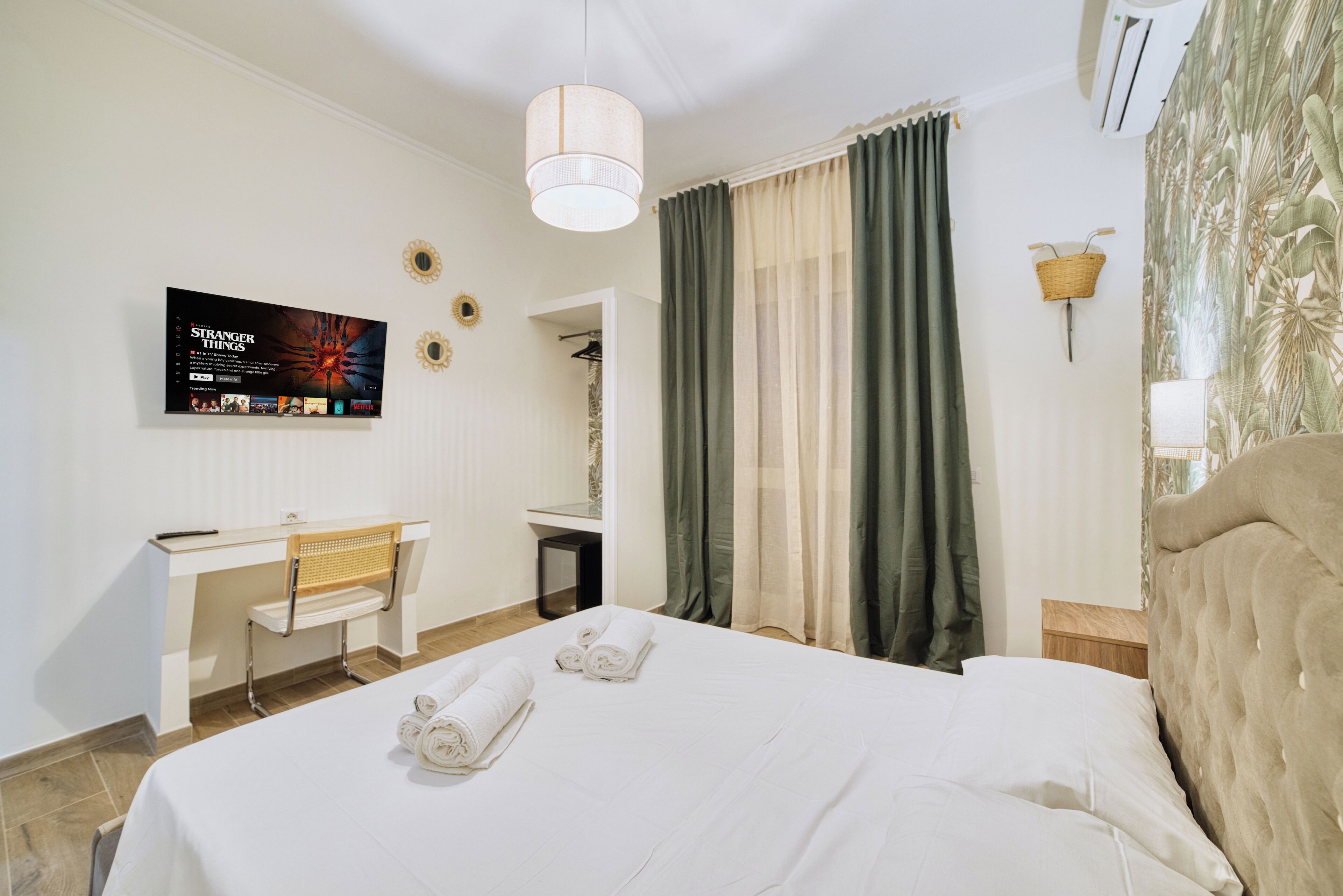 Une chambre d’hôtel comprenant un lit, un bureau, une chaise, un téléviseur fixé au mur et une fenêtre avec des rideaux.