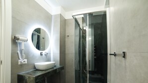A modern bathroom with a glass-enclosed shower, a round mirror with under-cabinet lighting, and a white sink on a marble countertop. - Radio Suites (Rome)