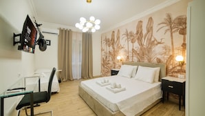 A hotel room with a bed, a desk with a chair, a TV mounted on the wall, and a tropical-themed wall mural. - Radio Suites (Rome)