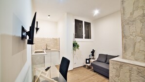 A modern living room with a sofa, a dining table with chairs, a TV mounted on the wall, and a stone accent wall. - Radio Suites (Rome)