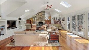 A spacious living room with a high ceiling, a stone fireplace, and a staircase leading to an upper level.