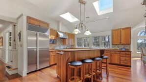 A modern kitchen with a central island, bar stools, and a stainless steel refrigerator.
