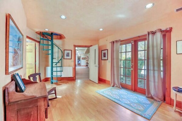 A spacious hallway with wooden flooring, a spiral staircase, and a large glass door leading outside.