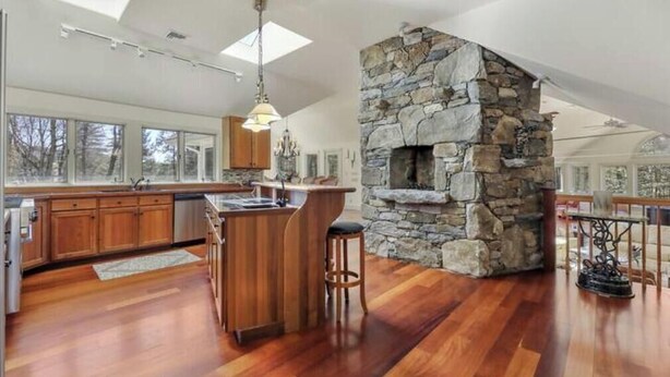 A spacious kitchen with a stone fireplace, wooden cabinets, and a large island.
