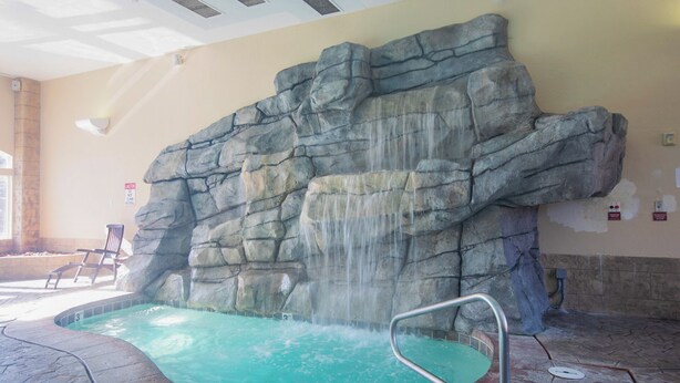 A hot tub area with a waterfall feature, a pool, and a caution sign on the wall. - Swiss-charmed Mountain Retreat NEW Listing (Midway)